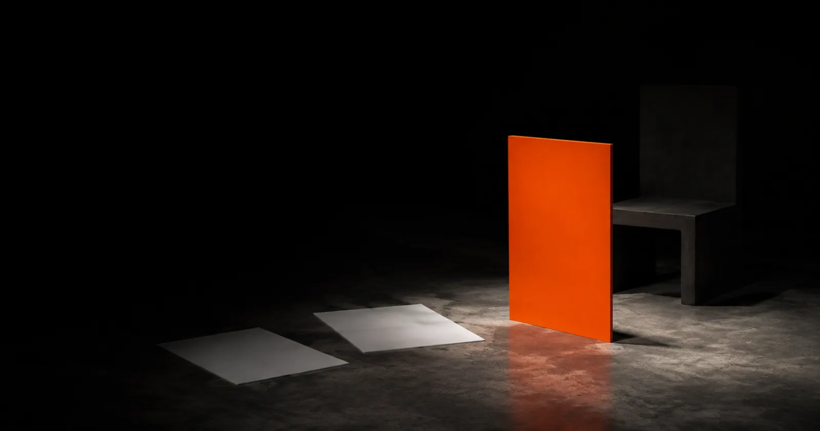An upright orange panel standing in the light in front of an empty concrete chair